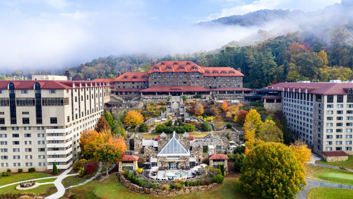 Aerial of full Omni Grove Park Inn buildings and grounds, full of fall foliage with mountains in background