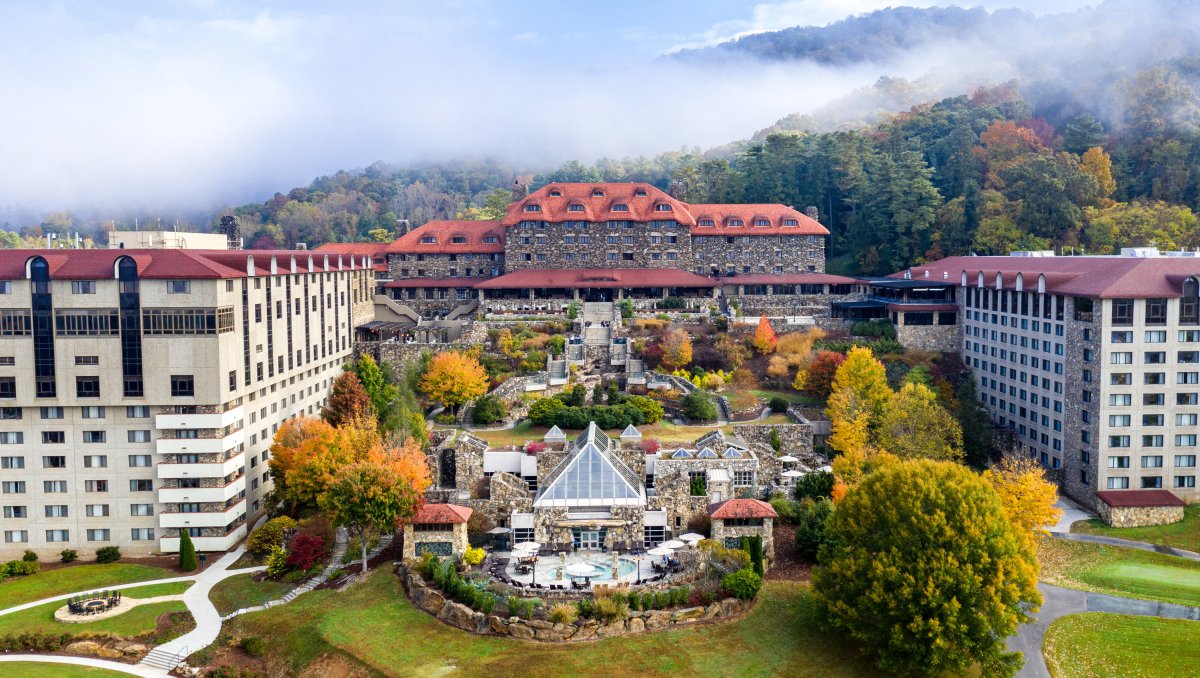 Aerial of full Omni Grove Park Inn buildings and grounds, full of fall foliage with mountains in background