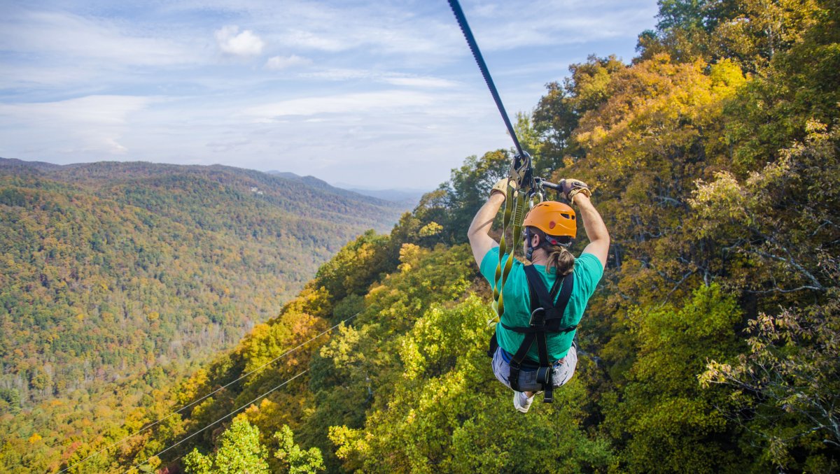 Person zip lining down cable and looking out over fall foliage-covered mountains during clear day