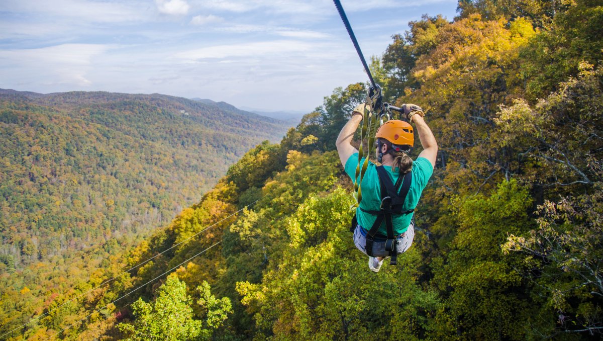 Person zip lining down cable and looking out over fall foliage-covered mountains during clear day