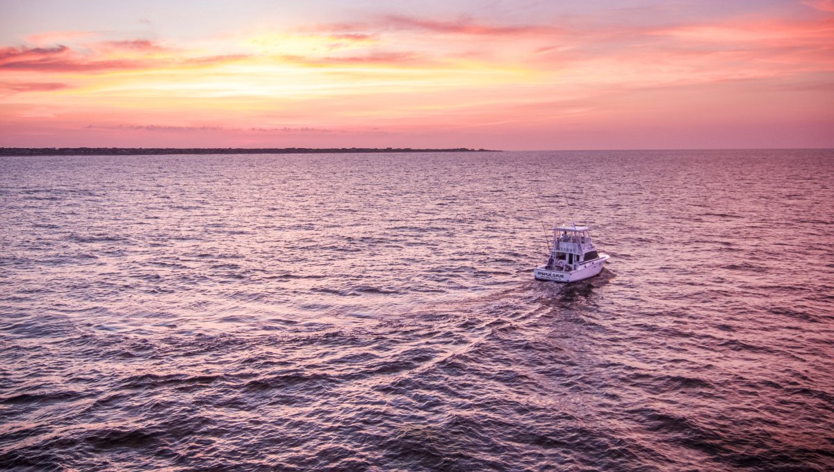 Aerial of fishing charter boat under beautiful pink and orange sky.