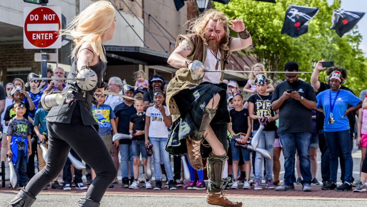Two actors dressed as pirates swordfighting with crowd watching in background