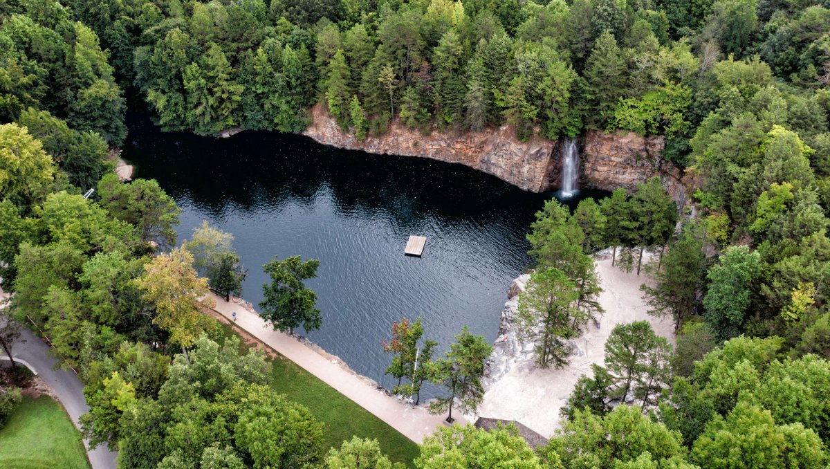 Aerial of quarry surrounded by trees with swimming platform in middle of water