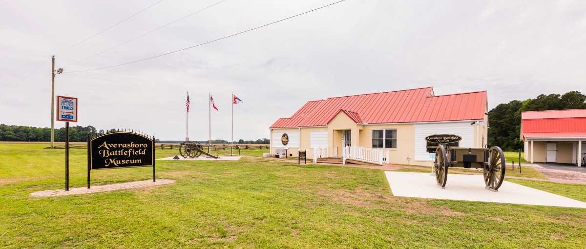 Exterior of Averasboro Battlefield Museum with signage, cannons and flags in front of museum