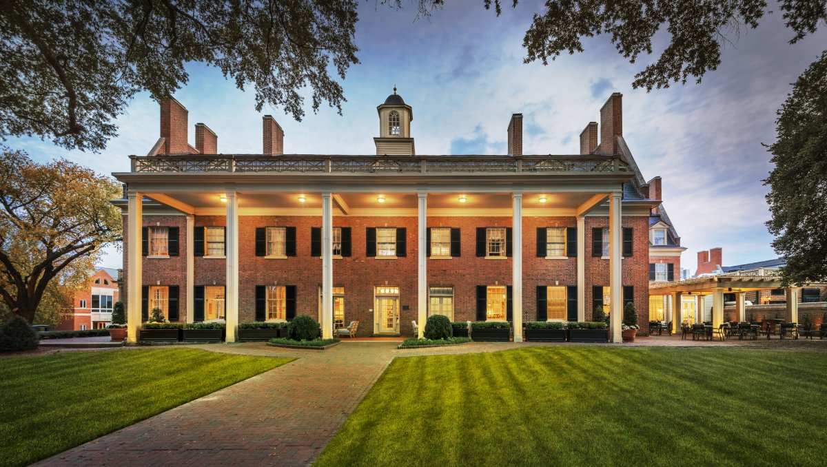 Exterior of grand, brick inn lit up at dusk with green grounds in foreground