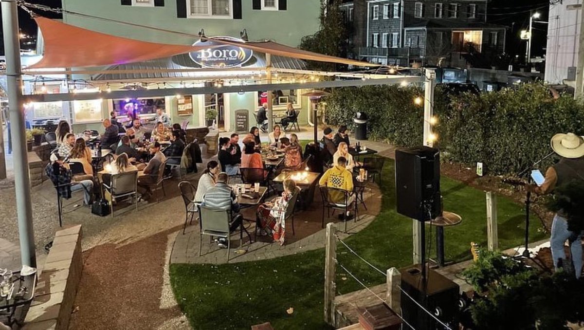 Diners sitting around firepits outside at night at coastal restaurant.