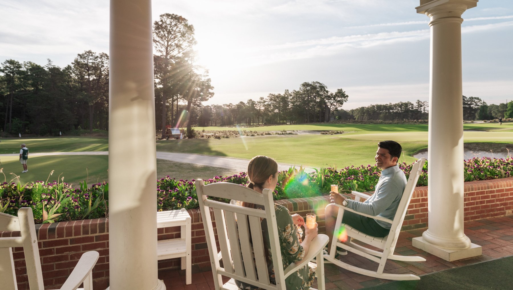 Couple enjoying cocktails in rocking chairs on patio overlooking Pinehurst Resort course.