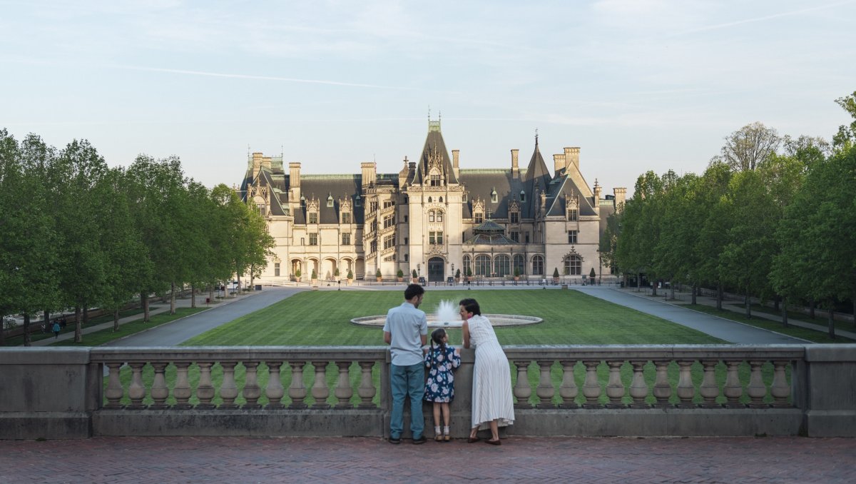 Family of 3 standing at stone wall overlooking Biltmore Estate and grounds