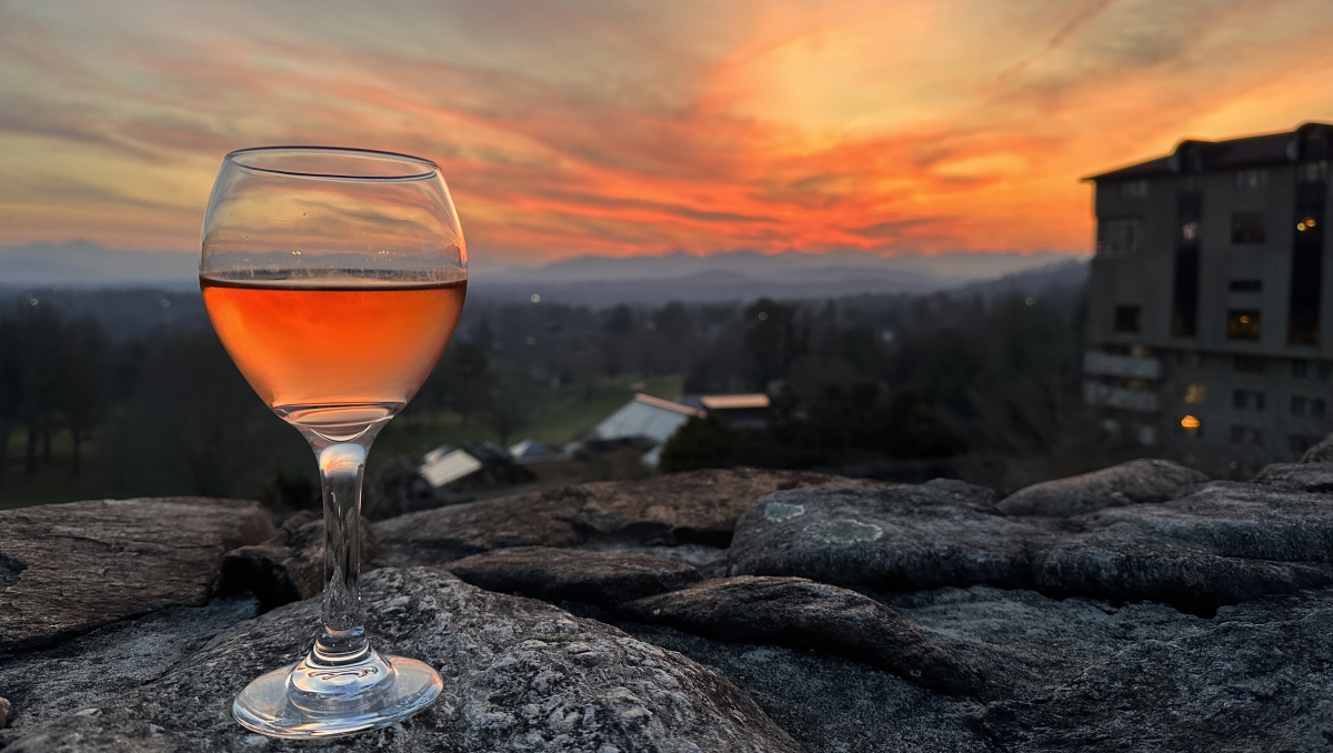 Glass of rose wine sitting on stone wall with hotel and blazing orange sunset in background