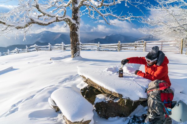 Man in winter gear sitting at snowy table with snow and mountains in background during daytime
