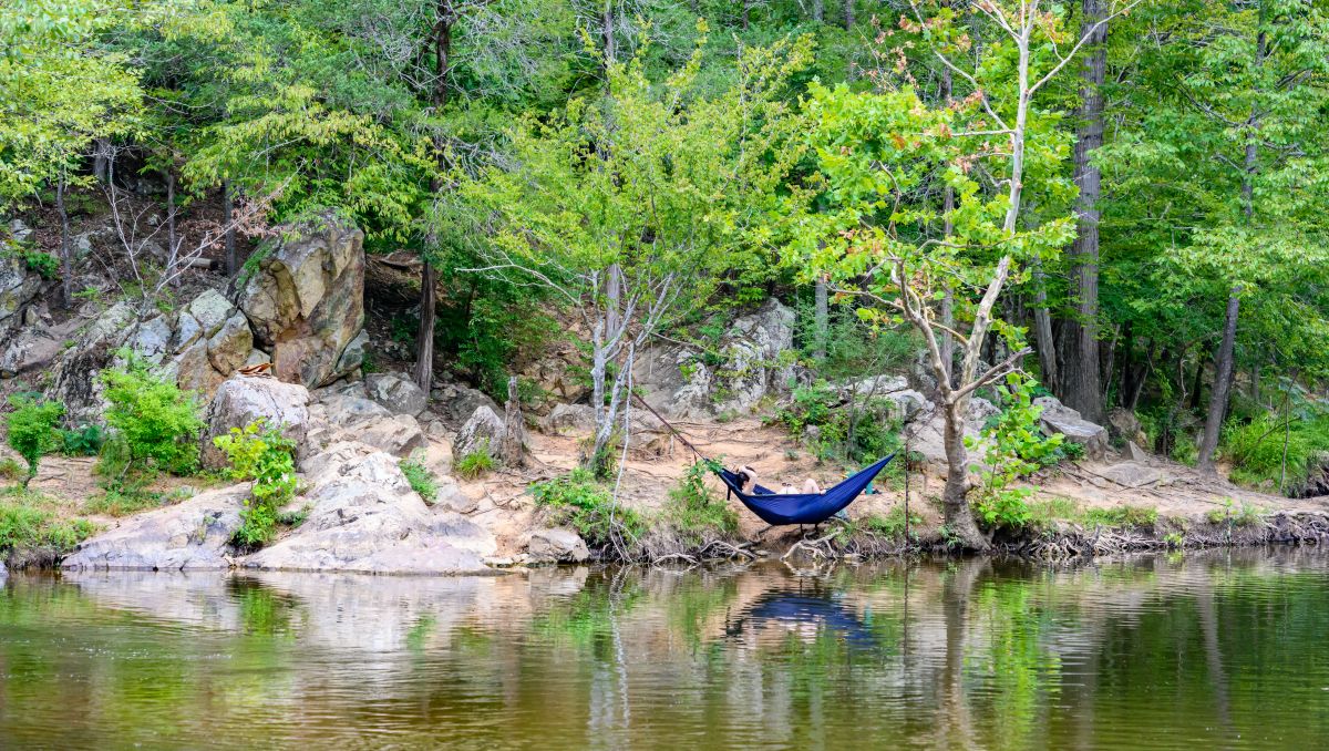 Person lounging in blue hammock with trees in background next to Sennett's Hole swimming hole