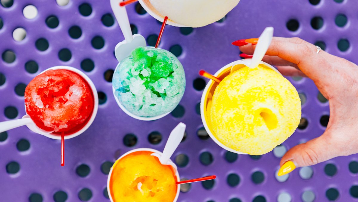 Hand reaching for snow cone on purple table surrounded by more snow cones