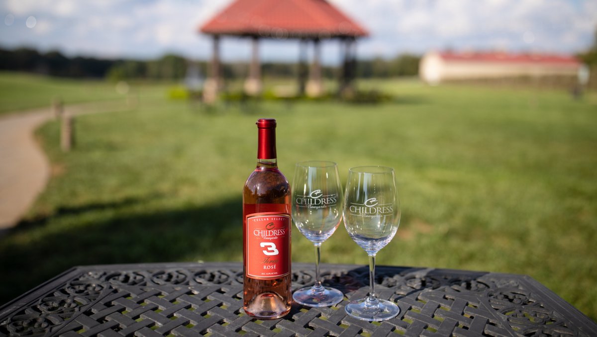 Bottle of Childress Vineyards wine and two wine glasses on table with gazebo in background