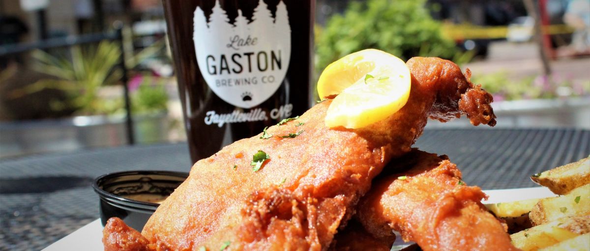 Fish and chips on a plate in front of a pint of dark beer during daytime