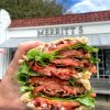 Hand holding huge BLT Sandwich in front of restaurant