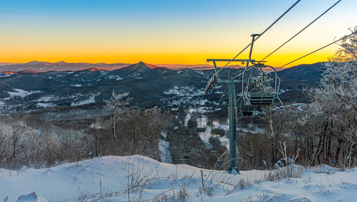Orange sunrise over mountain range with snow and ski lift in foreground
