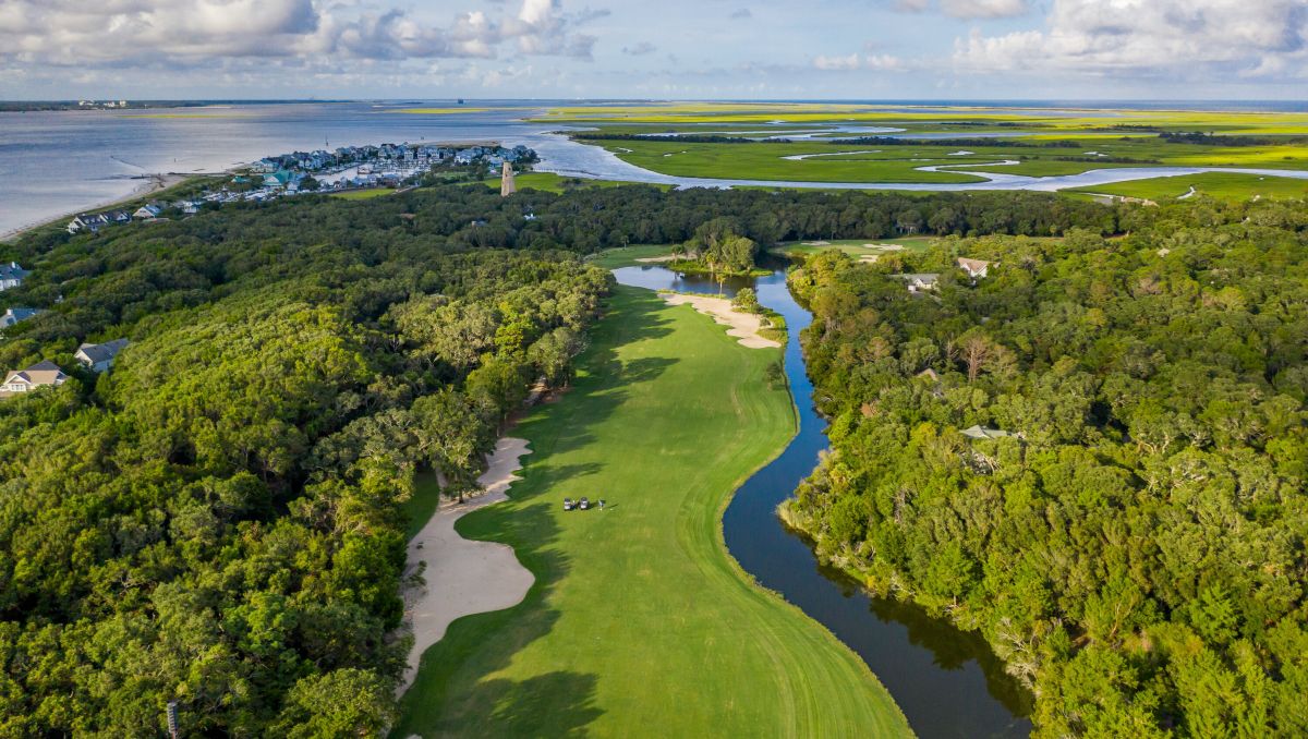 Aerial view of Bald Head Island Golf Club's golf course with trees, Old Baldy and waterways during daytime