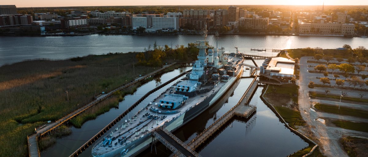Aerial shot of Battleship North Carolina in river with city in background during daytime.