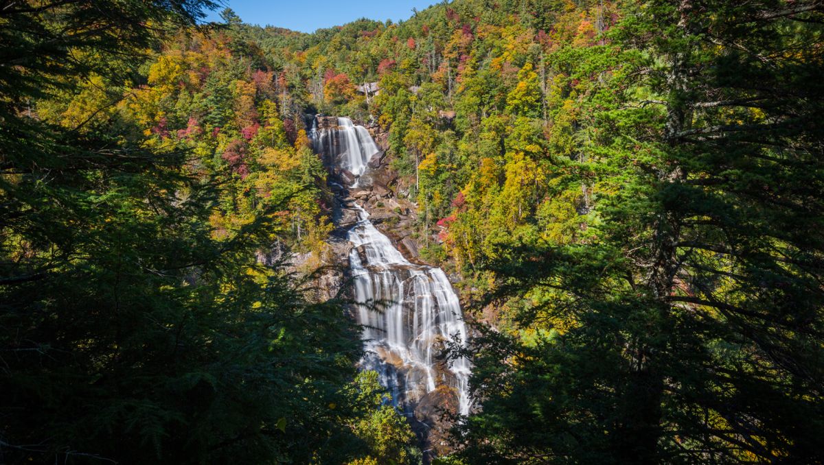 Faraway view of huge waterfall cascading down in middle of fall foliage