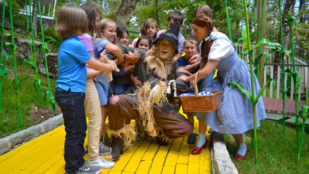 Kids and Dorothy surrounding the Scarecrow on the Yellow Brick Road at Land of Oz theme park