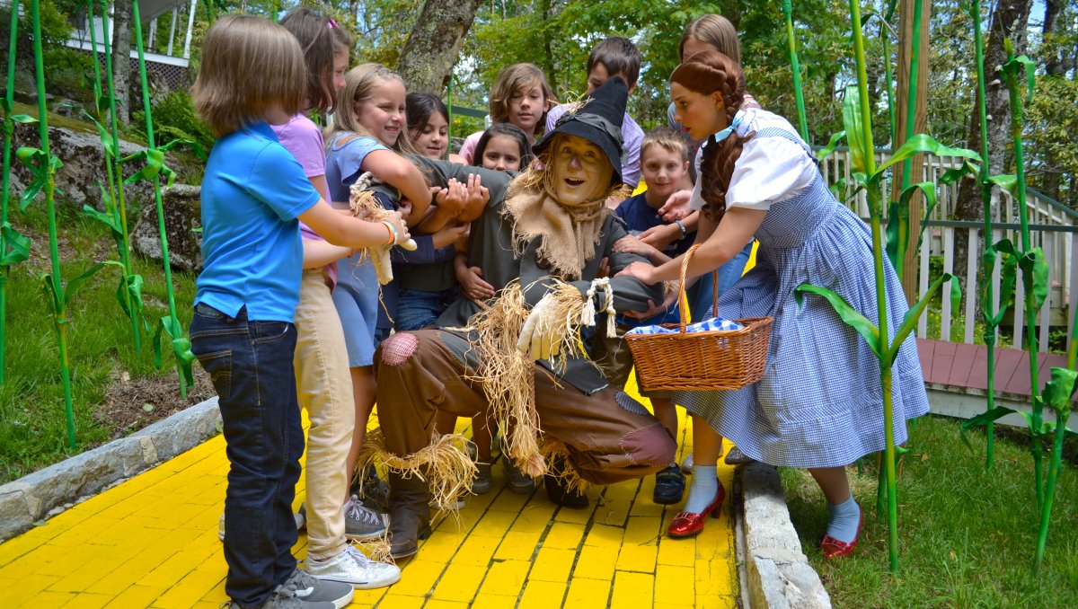 Kids and Dorothy surrounding the Scarecrow on the Yellow Brick Road at Land of Oz theme park