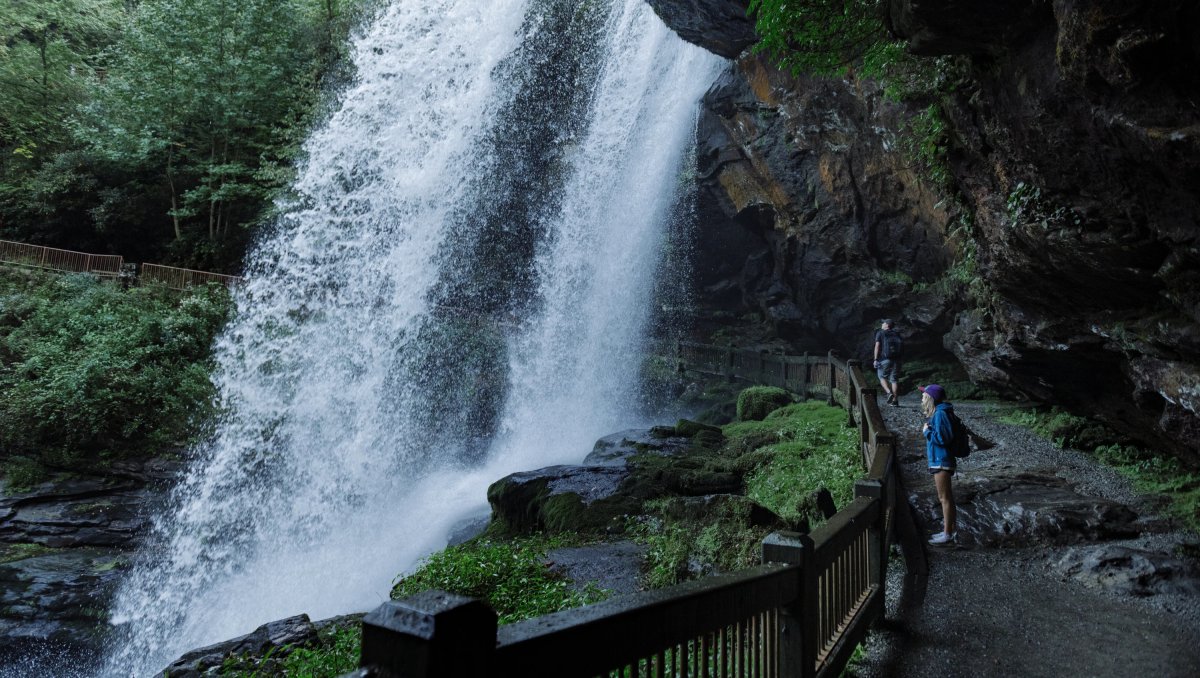 Woman standing in walking path behind and under large waterfall